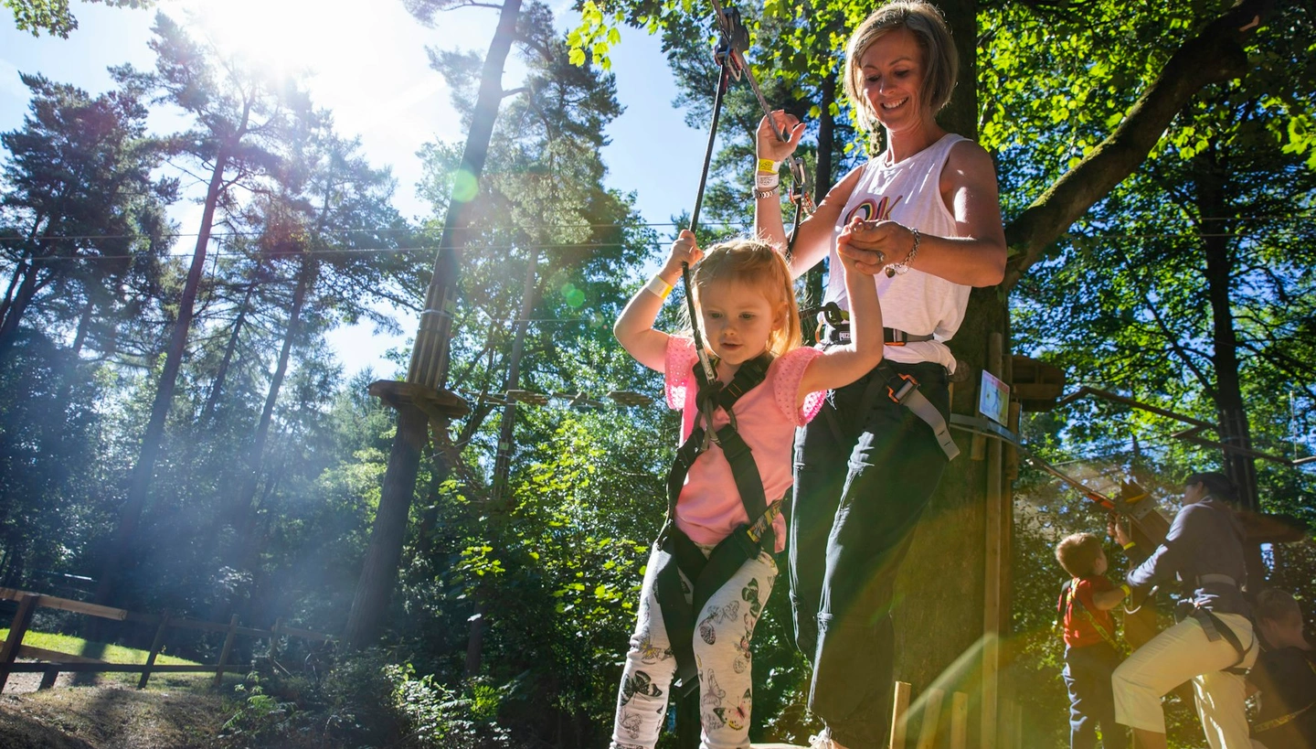 A young girl and her mum hold hands as she negotiates a ropes crossing.