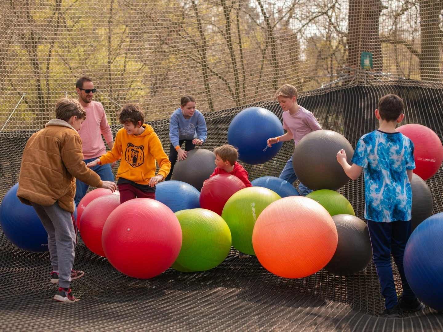 Group playing on a giant net suspended between trees with giant inflatable balls.
