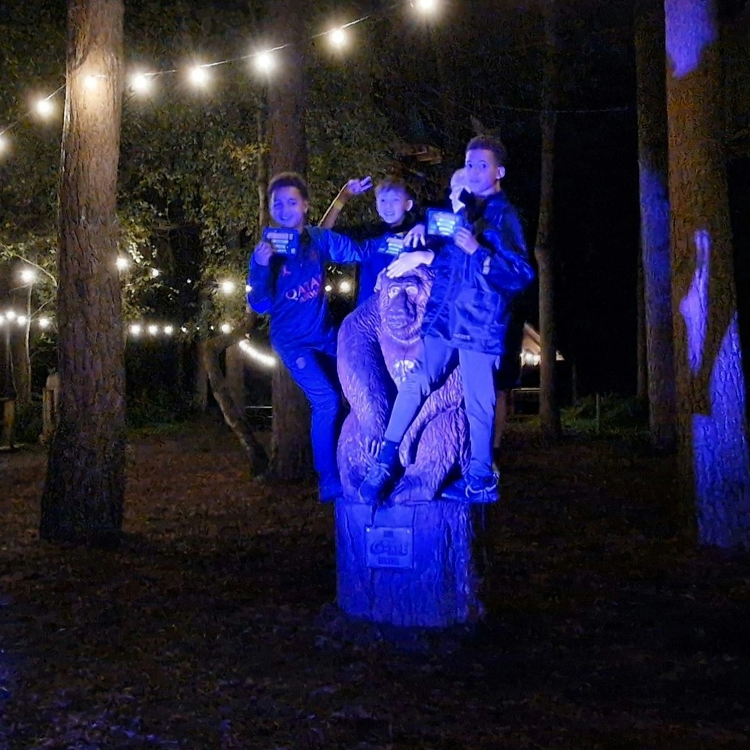 Children celebrate their Sundown Adventure with a photo by the Go Ape wooden gorilla lit with coloured lights