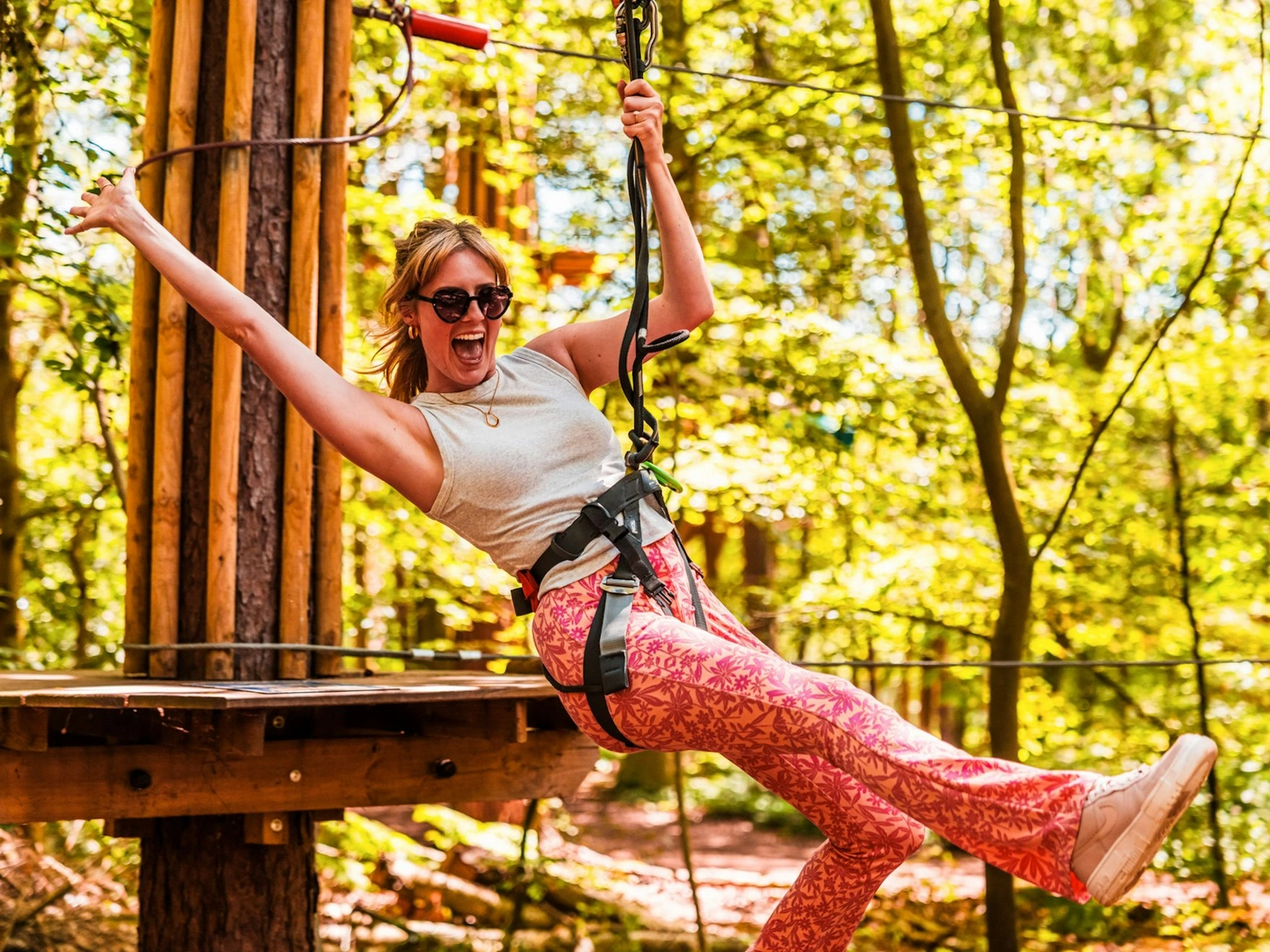 A woman throws out her arm and smiles as she goes down a zip wire